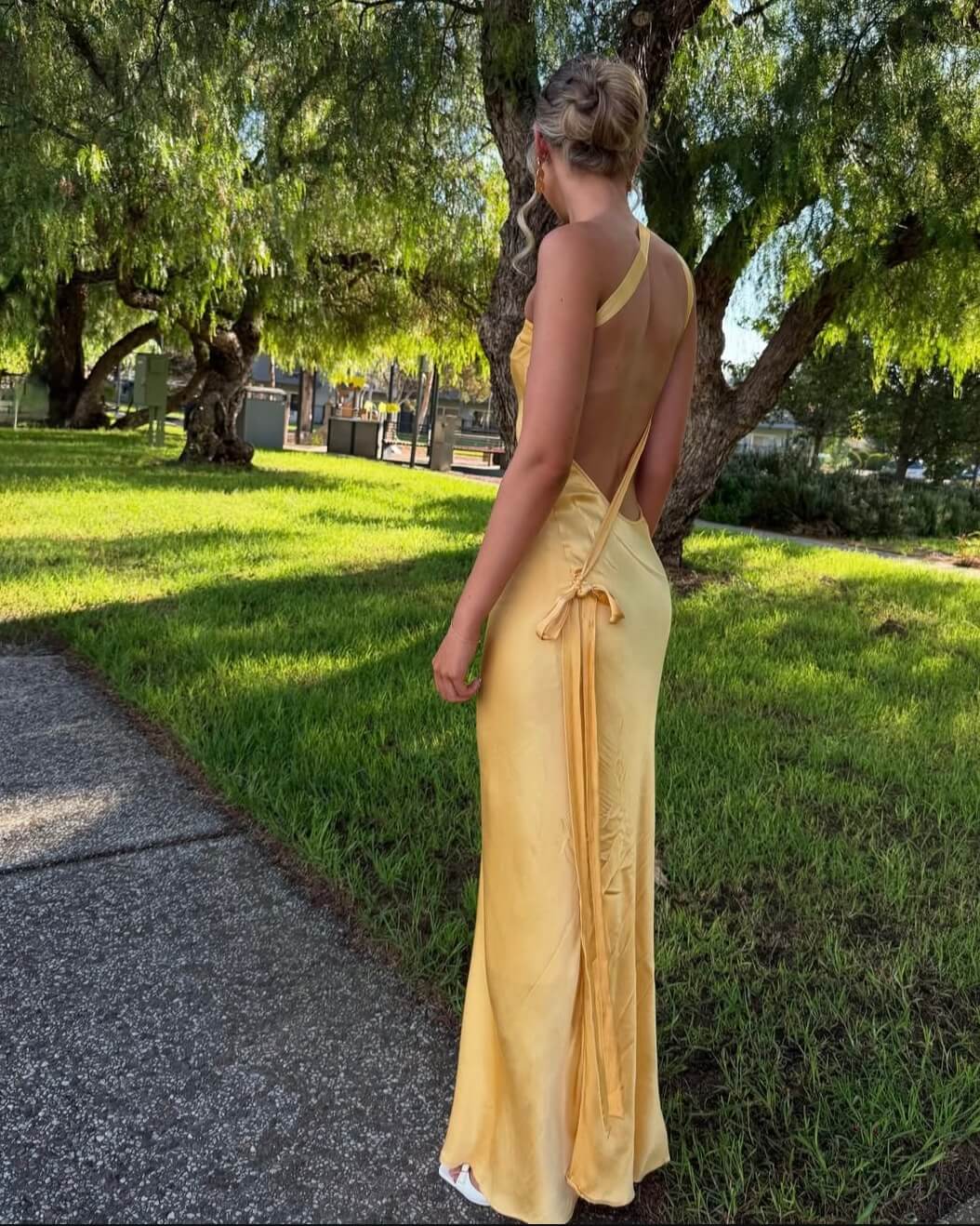 Person wearing a yellow dress with an open back and side slits, rocking a green based fake tan